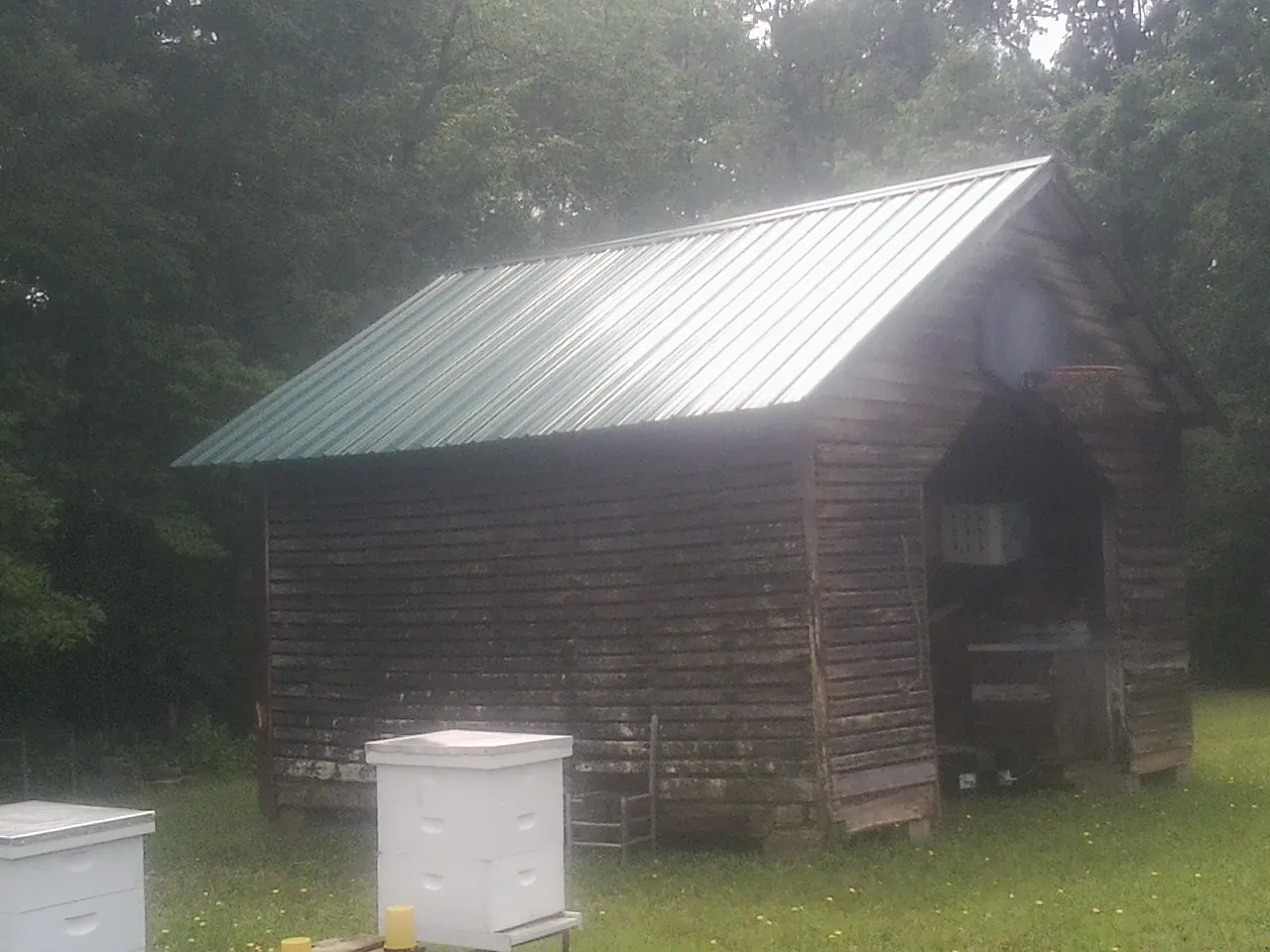 Green metal roof on a weathered barn beside stacked beehives in Stone Ridge