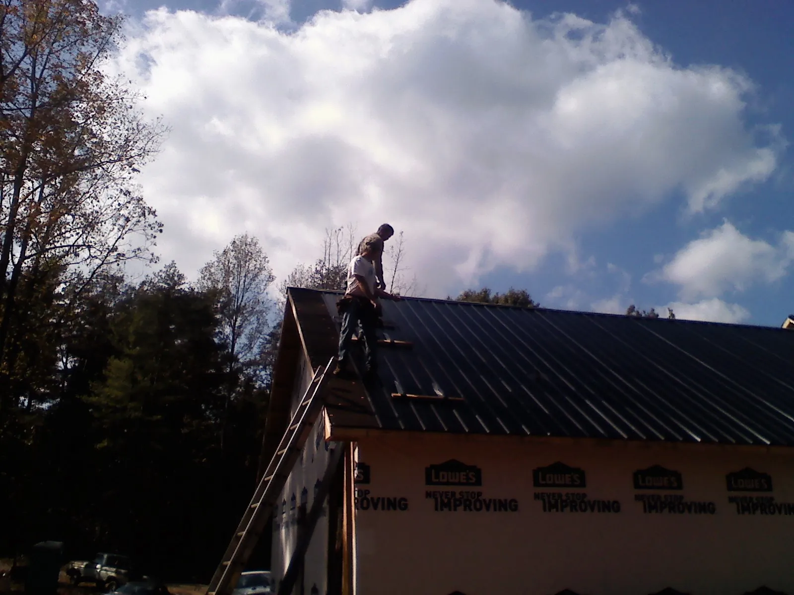 Roofer fastening dark metal panels high against a cloudy sky, from a Roof Inspection job in Stone Ridge