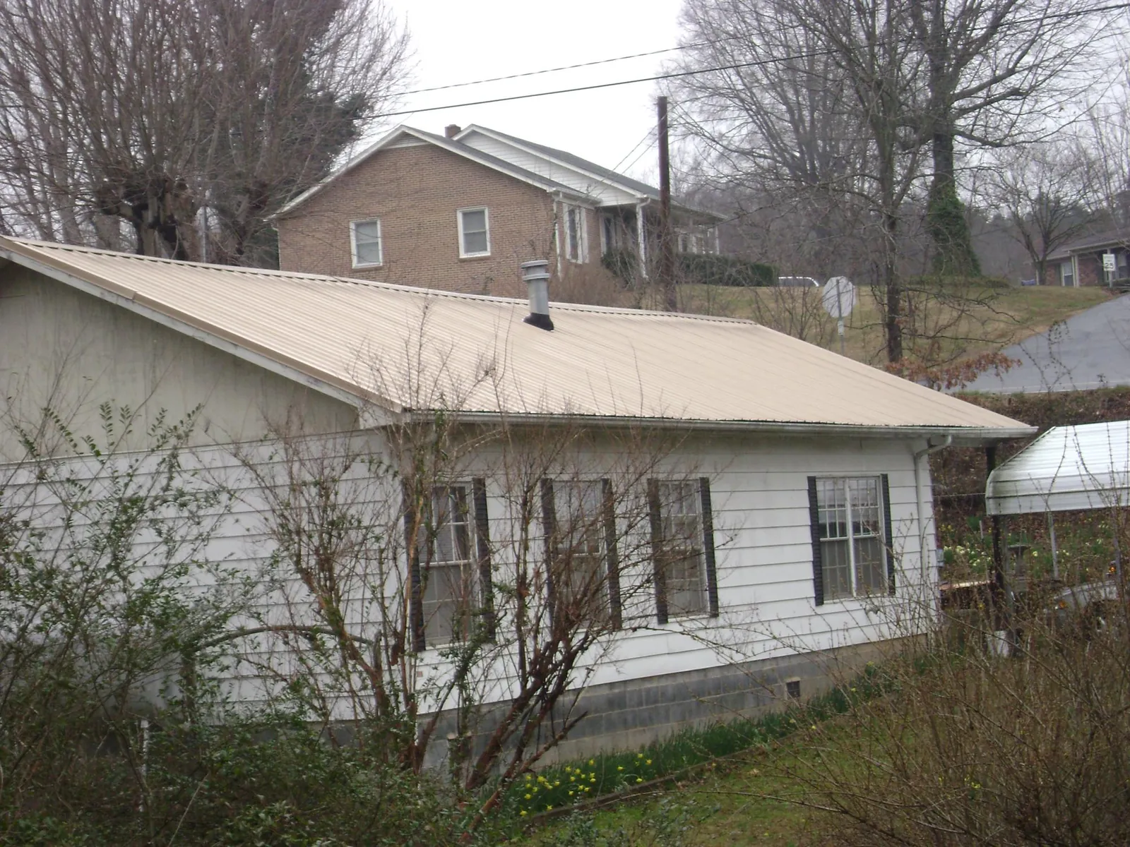 Tan metal roof on a white sided house set into a hillside — Commercial Roofing by Roofing Brothers in Stone Ridge