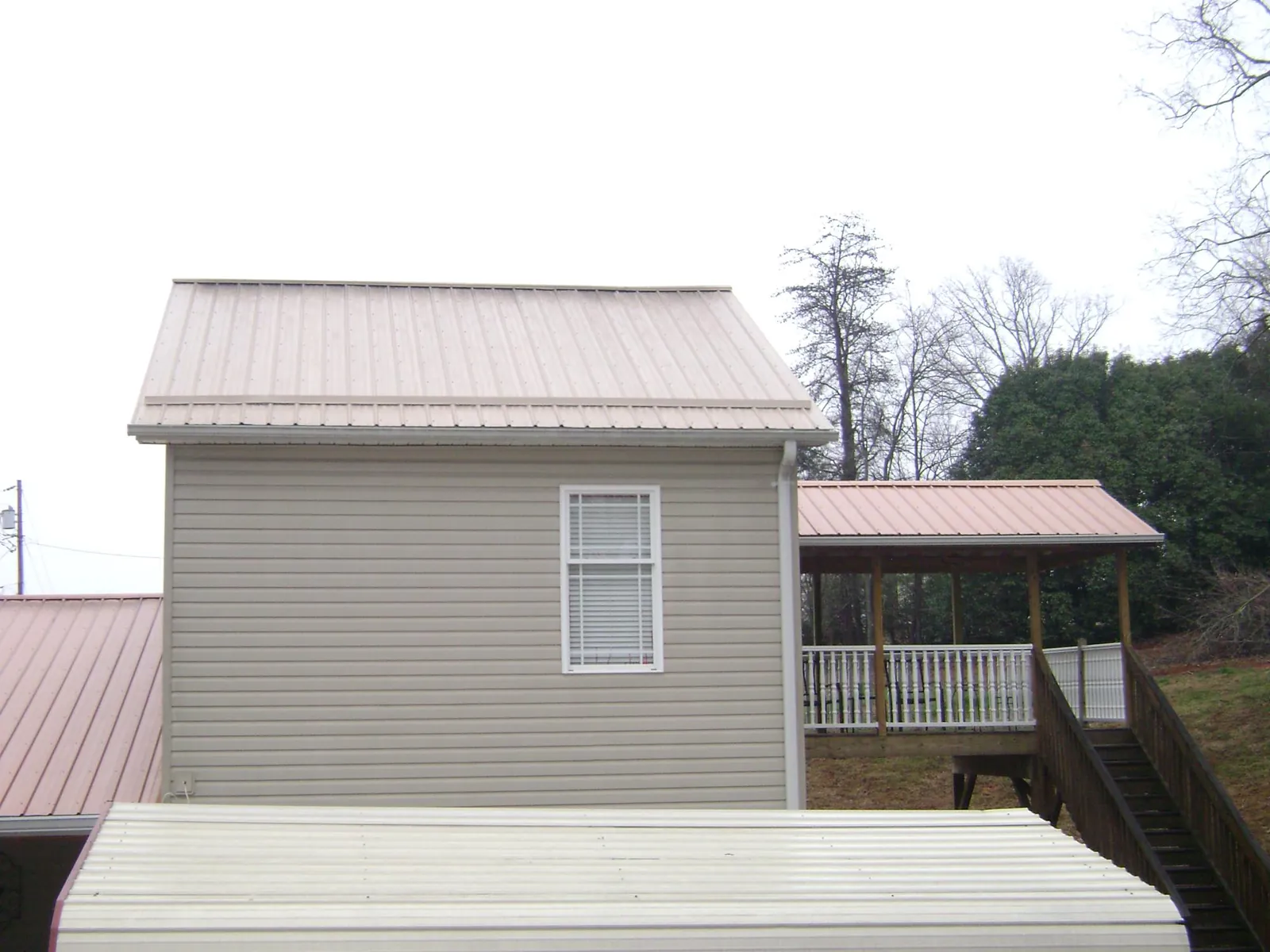 Tan metal roofs on a two story addition and attached porch, from a Roof Replacement job in Stone Ridge